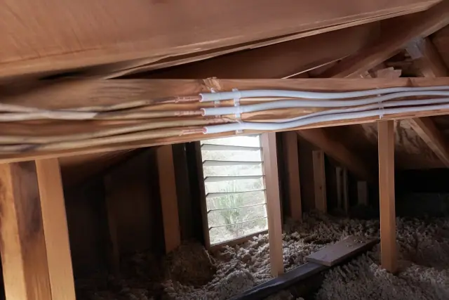 New copper wiring and connectors installed along wooden attic rafters during a home rewiring project in Phoenix, AZ.
