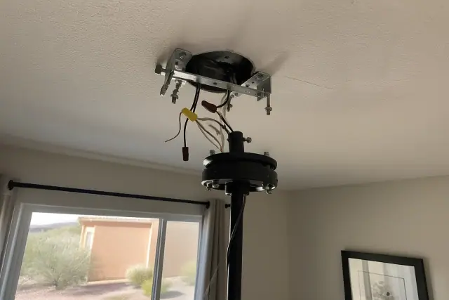 Electrician installing a ceiling fan mounting bracket and wiring in a residential living room in Mesa, AZ.
