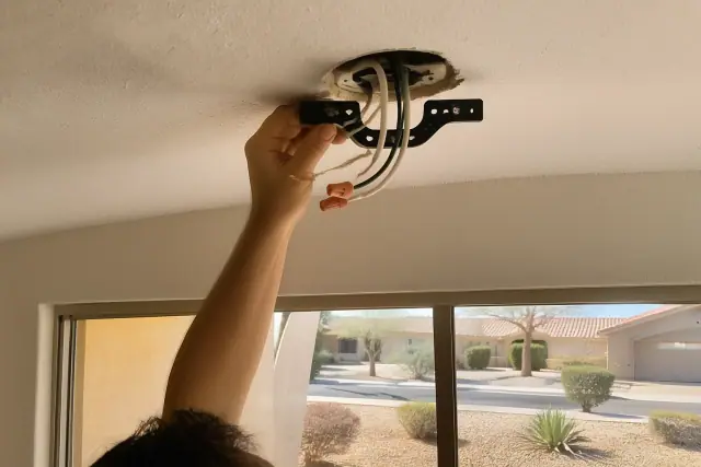 Electrician installing a ceiling fan mounting bracket and wiring in a Peoria, AZ home.