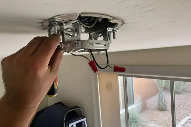 Electrician installing a ceiling fan mounting bracket and wiring in a Sun City, AZ home.