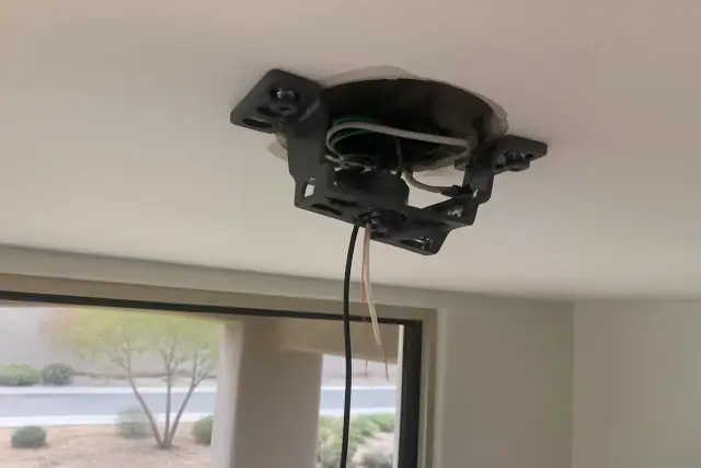 Electrician installing a ceiling fan mounting bracket and wiring in a room in Chandler, AZ.