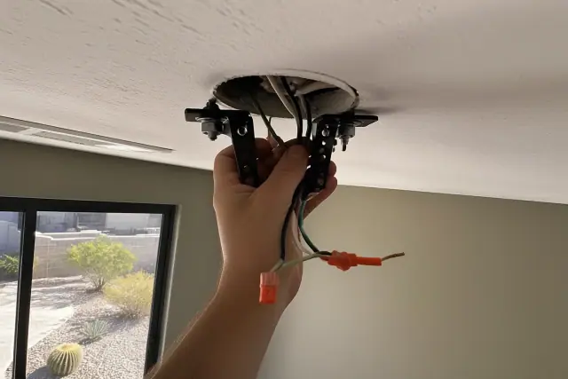 Electrician installing a ceiling fan mounting bracket and wiring in a home in Gilbert, AZ.
