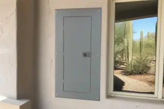 Closed electrical panel on a stucco wall with a view of desert cacti in Phoenix, AZ.