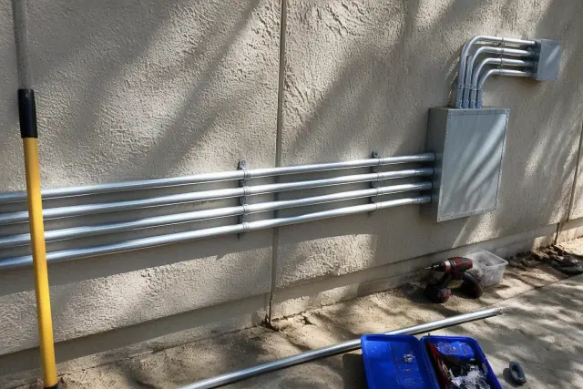 Exposed metal conduit and a junction box on a stucco wall at an industrial worksite in Phoenix, AZ.