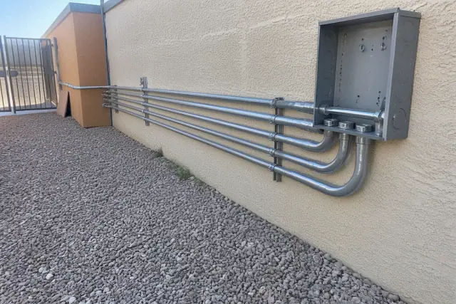 Exposed metal electrical conduit and a junction box on a stucco wall at a project site in Chandler, AZ.
