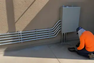 Metal conduit pipes and a junction box on a stucco wall during a job site cleanup in Phoenix, AZ.