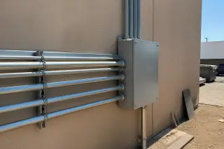 Metal conduit pipes and a junction box mounted on a stucco wall at an industrial worksite in Phoenix, AZ.