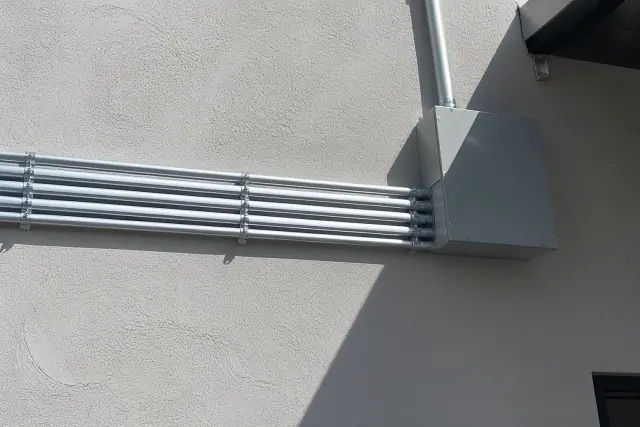 Exposed metal conduit pipes leading to a junction box on a stucco wall at a commercial lighting installation in Phoenix, AZ.