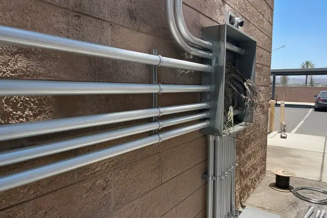 Exposed electrical wiring and conduit pipes on a stucco wall at a commercial job site in Phoenix, AZ.