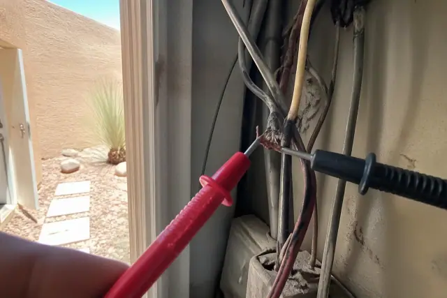 Multimeter probe testing frayed wires inside a residential utility closet during an electrical repair in Glendale, AZ.