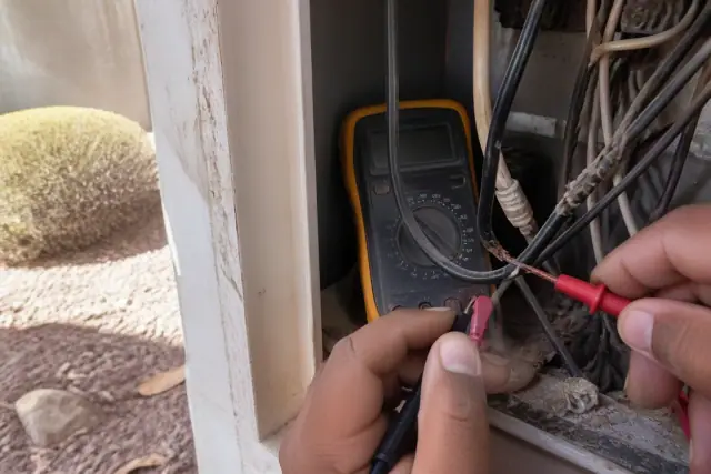 Multimeter probe testing continuity on damaged wires inside a residential utility closet in Tempe, AZ.