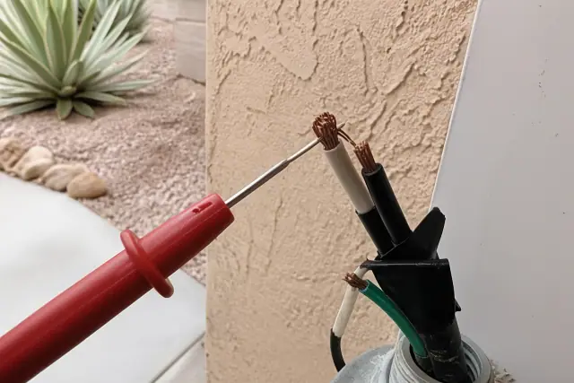 Multimeter probe testing damaged electrical wiring outside a stucco home in Sun City, AZ.