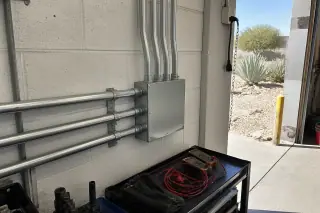 Metal electrical junction box with conduit pipes in a Phoenix, AZ workshop.