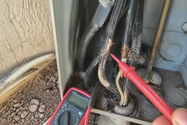 Multimeter probe testing damaged wires in a utility area at a worksite in Phoenix, AZ.