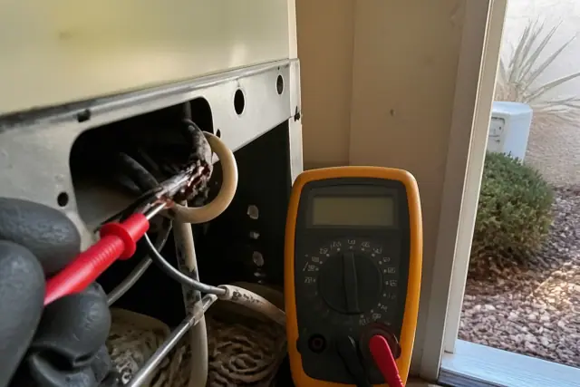 Multimeter probe testing damaged wires in a residential utility closet in Glendale, AZ.