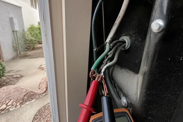Multimeter probe testing damaged wires in a residential utility closet during an electrical repair in Phoenix, AZ.