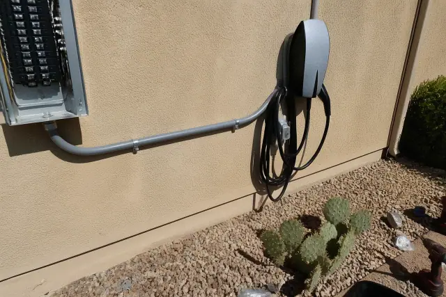 Technician installing an EV charger on a stucco wall with conduit and prickly pear cactus in Phoenix, AZ.