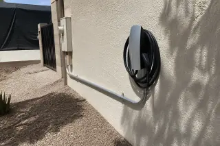 Wall-mounted EV charger with metal conduit on a stucco wall at a home in Phoenix, AZ.