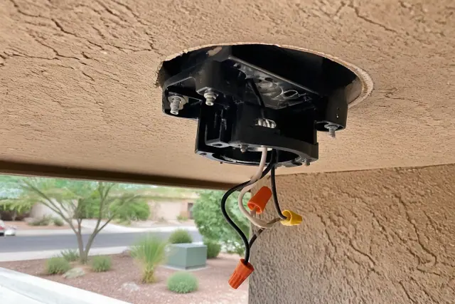 Technician installing a ceiling fan mounting bracket and wiring on a stucco wall in Phoenix, AZ.
