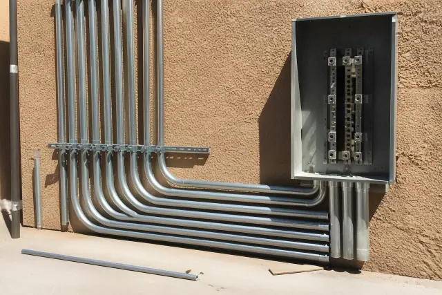 Exposed metal conduit pipes and a junction box on a stucco wall at an electrical jobsite in Phoenix, AZ.