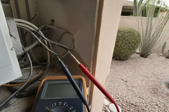 Multimeter testing damaged wires during ceiling fan circuit troubleshooting in a Phoenix, AZ utility closet.