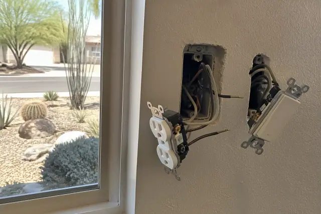 Electrical wiring and outlet installation in a wall box at a home in Phoenix, AZ, with a view of a xeriscaped yard.