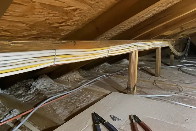 Bundles of electrical cables stapled to wooden rafters during a home rewiring project in an attic in Scottsdale, AZ.