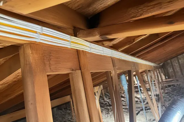 Bundle of non-metallic sheathed electrical cables stapled along wooden attic rafters during a rewiring in Gilbert, AZ.