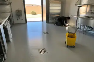 Technician using a work light to inspect epoxy kitchen floor drains in a Phoenix, AZ commercial space.