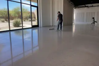 Technician sweeping dust from a polished concrete retail floor in Phoenix, AZ, with desert scenery outside.