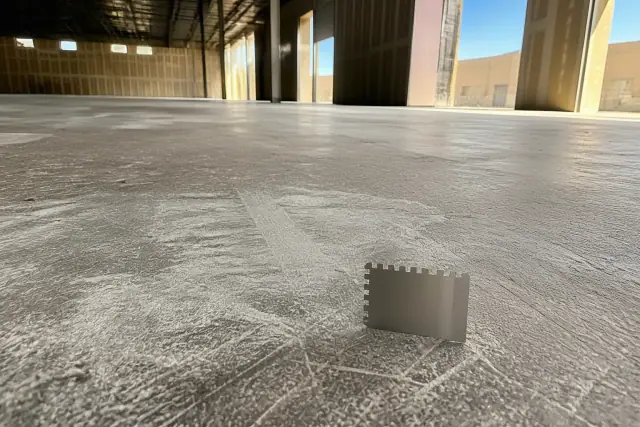 A wet-film gauge resting on a diamond-ground concrete floor inside a Phoenix, AZ warehouse.