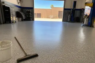 Epoxy flake floor in a vehicle workshop in Phoenix, AZ, with a cleanup broom and pail near the open bay door.