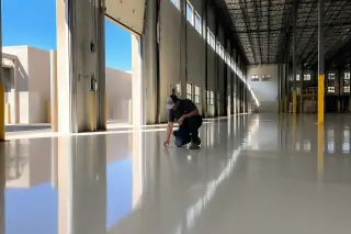 Worker inspecting a high-gloss resin floor in an industrial warehouse under sunlight in Phoenix, AZ.