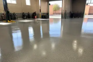 High-gloss industrial epoxy floor in an automotive workshop in Phoenix, AZ, with heavy equipment and desert sunlight.