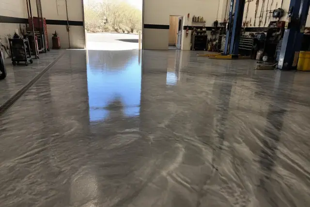 Metallic epoxy floor in an automotive workshop in Phoenix, AZ, with sunlight streaming through an open bay door.