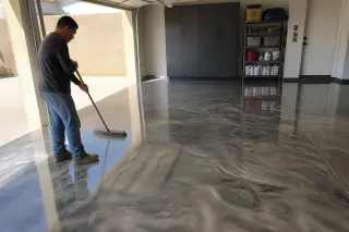 Technician sweeping a metallic epoxy floor in a residential garage with desert light in Phoenix, AZ.