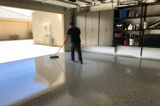 Technician sweeping a high-gloss epoxy floor in a Phoenix, AZ garage with bright desert sunlight at the door.