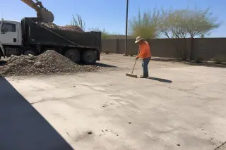 Worker sweeping concrete fragments from a cleared construction site in Phoenix, AZ.