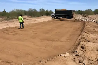 Worker inspecting freshly leveled and raked soil in a cleared loading area in Phoenix, AZ.
