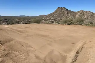 Smoothly graded dirt pad with native creosote bushes on a sloped desert site in Phoenix, AZ.