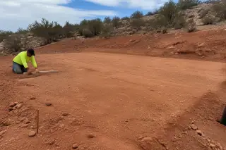 Technician checking the level of a compacted dirt pad near creosote bushes in Phoenix, AZ.