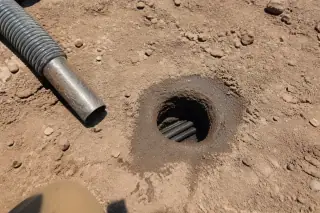 Small circular hole excavated in desert soil with a vacuum hose nozzle at a Phoenix, AZ worksite.