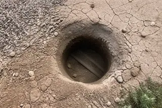 Circular hole excavated in sun-baked desert soil revealing underground cables in Phoenix, AZ.