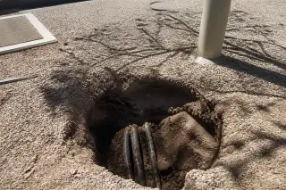 Small circular excavation hole with exposed underground cables in rocky desert soil in Phoenix, AZ.