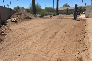 Worker inspecting a filled-in earth pit with heavy equipment tracks at a construction site in Phoenix, AZ.