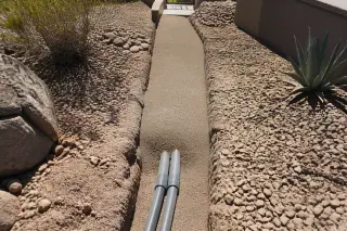 Finished underground utility conduits and backfilled trench in rocky desert soil at a construction site in Phoenix, AZ.