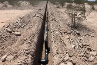 Utility pipes installed in a straight trench through rocky desert soil in Phoenix, AZ.