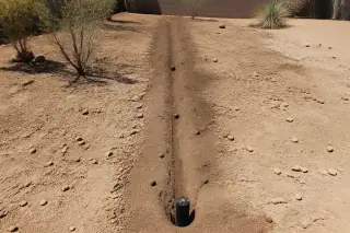 Narrow utility trench with exposed pipes in backfilled rocky soil on a Phoenix, AZ construction site.