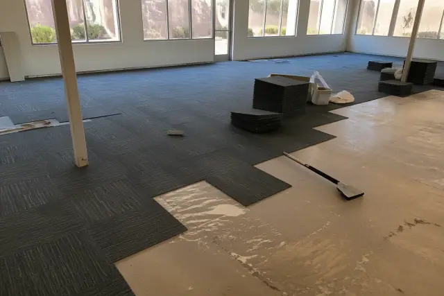 A worker installing modular carpet tiles in an Avondale, AZ workspace with desert views visible through the windows.