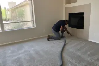 Technician vacuuming and inspecting new carpet flooring in a residential living room in Phoenix, AZ.